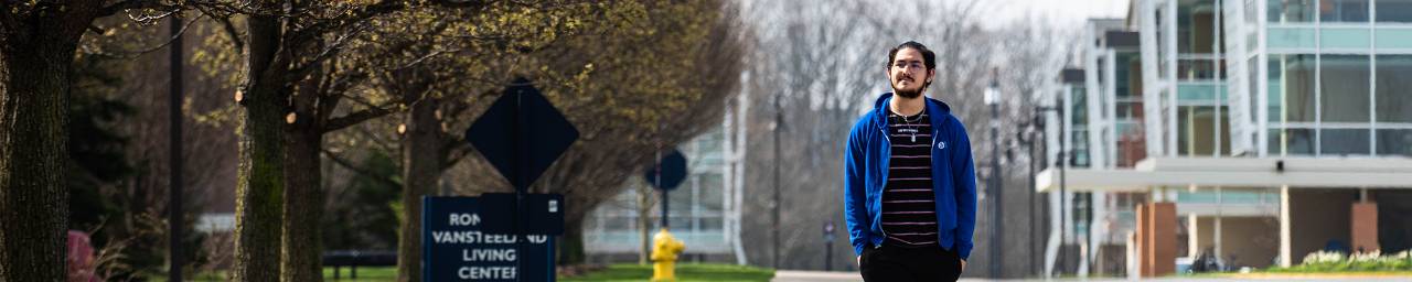 A student, Renzo Garza Motta, walks in front of the Ron Van Steeland Living Center on GVSU's Allendale Campus.